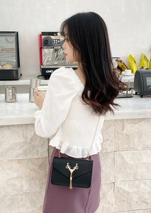 Model wearing a black leather envelope crossbody bag with a golden deer head and tassel