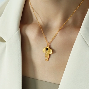Golden elephant pendant necklace with black gemstone detail worn on a white blazer