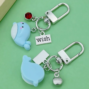 Blue resin dolphin keychain with wish metal tag and red gemstone charm on light green background