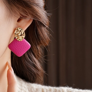 Close-up of model wearing irregular gold metal and fuchsia leather geometric earrings