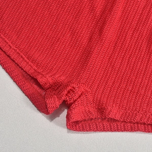 Close-up of bright red knit bodysuit showing precision stitching and chevron texture