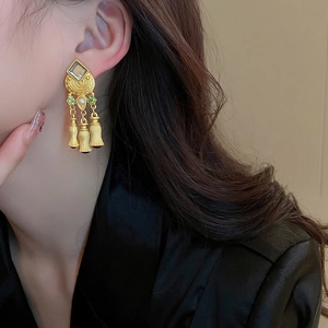 Golden vintage fringe earrings with green gemstones worn by a model in a close-up shot