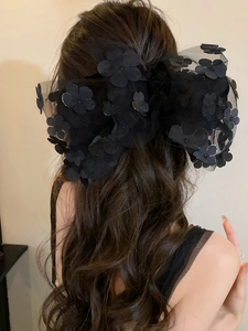 Detail of a large black mesh hair bow clip featuring 3D floral accents on long hair