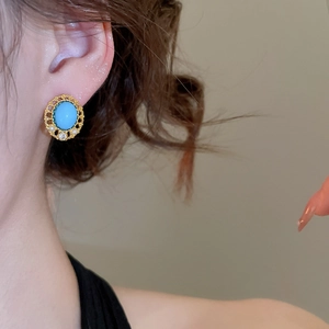 Close-up of a model wearing vintage gold earrings with oval turquoise and pearl accents