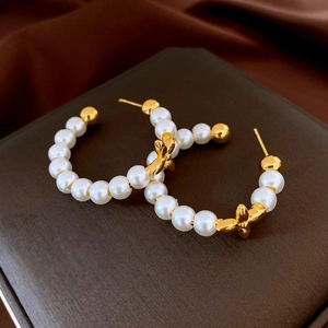 Close-up of pearl hoop earrings with a gold bow accent on a dark leather display