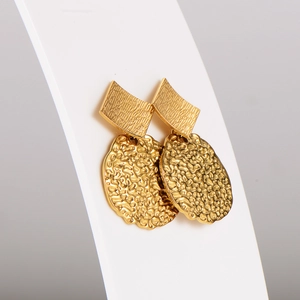 Detail of gold metal earrings with hammered texture and square geometric pattern