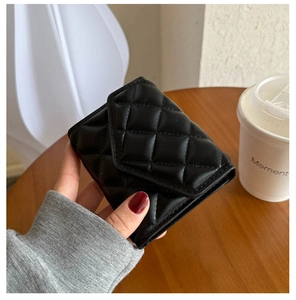 Close-up of a black quilted leather mini purse held against a clean desktop background