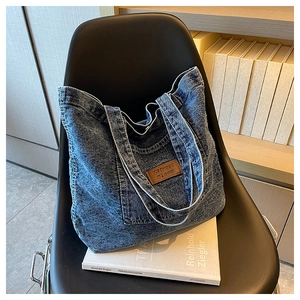 Detail of blue washed denim tote bag showing brown leather patch on a black chair