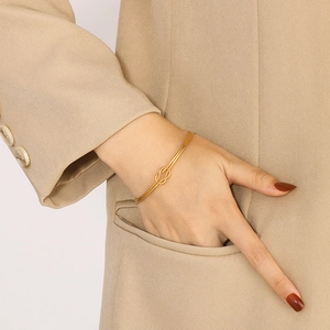 Bracelet jonc noué doré minimaliste porté avec une tenue de bureau beige élégante
