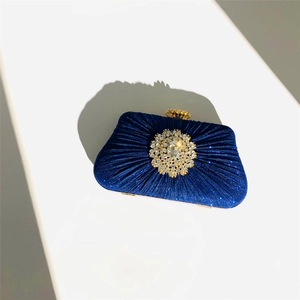 Detailed view of deep blue pleated satin evening clutch with round crystal floral ornament