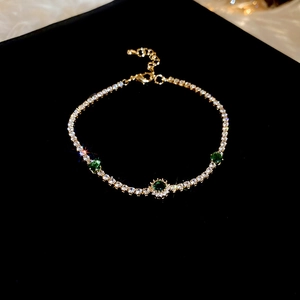 Détail du bracelet doré avec trois pierres vertes et zircons sur fond noir poli