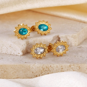 Golden sunflower earrings with turquoise and white stones on beige textured stone slabs