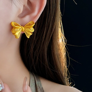 Macro shot of gold bow-shaped stud earring with hollow patterns on model's ear