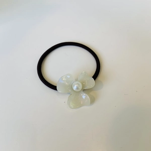 Detailed macro view of pearlescent flower hair tie with pearl center on black elastic band