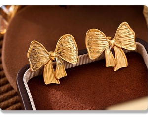 Close-up of golden bow earrings with brushed texture on a brown velvet jewelry box