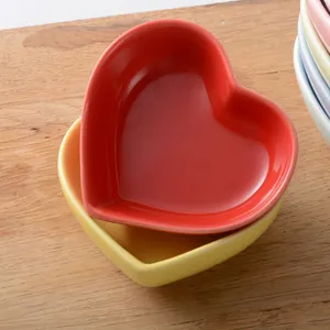 Stack of colorful heart-shaped ceramic dipping bowls in bright red and yellow on wood