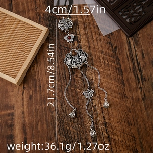 Detailed view of silver Chinese fan brooch with red gemstone and tassel on wooden surface