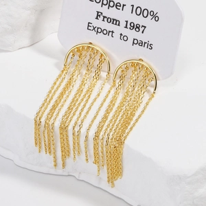 Detail of gold-plated copper tassel earrings displayed on a white textured stone base