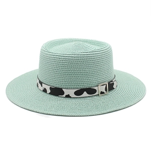 Detailed texture of mint green boater straw hat with cow print ribbon and silver buckle