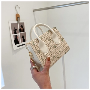 Detail of hand-woven straw bag featuring green leaf embroidery and premium leather handles