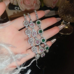 Close-up of three luxury tennis bracelets with emerald, pink, and white square stones