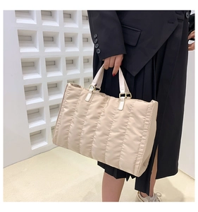 Close-up of quilted beige tote bag featuring gold square buckles and padded nylon texture