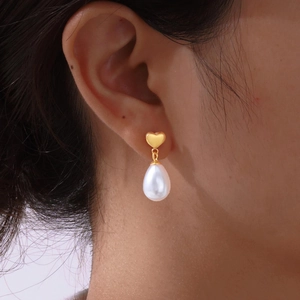 Close-up of elegant gold heart earrings with white teardrop pearl on a female model