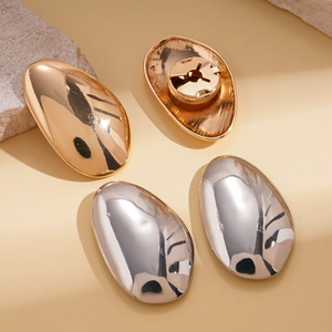 Macro shot of oval smooth metallic earrings in gold and silver finish on leather