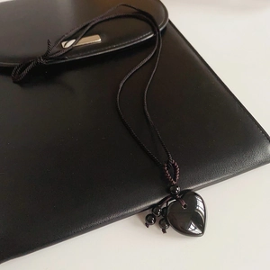 Macro detail of obsidian heart pendant with brown woven cord on leather surface