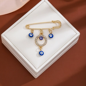Detailed view of gold safety pin brooch with blue evil eye charms and rhinestones