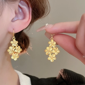 Elegant gold flower drop earrings with brushed metal texture worn by a model
