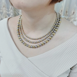 Detail view of triple-layered gold and silver polished bead necklace on model