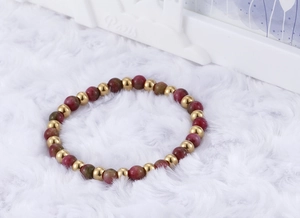 Detail of beaded gold steel bracelet with red and green stones on white fur background