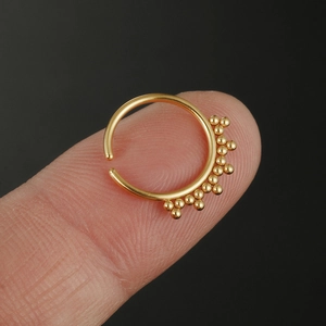 Anello al naso in acciaio inossidabile dorato con sfere mostrato su un dito sfondo