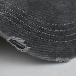 Detailed close-up of distressed denim texture and white stitching on a dark grey ponycap