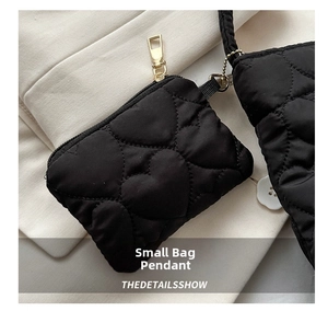 Macro detail of black heart-quilted accessory pouch with gold zipper and bead chain link