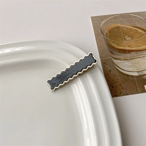 Close-up of a minimalist black hair clip with wavy white edges on a white porcelain dish