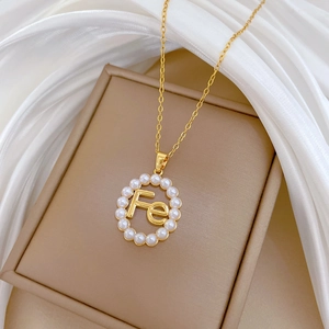 Macro detail of gold necklace with pearl circle pendant featuring Fe letter design