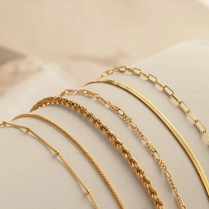 Detail of six gold layered chain bracelets featuring figaro, snake, and rope textures