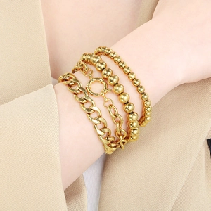 Detail of four-piece layered gold metal bracelet set with Cuban and bead chains on wrist
