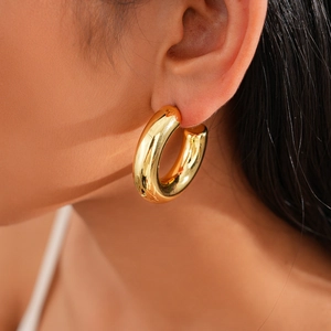 Close-up of chunky gold hoop earrings with a polished finish worn on ear model