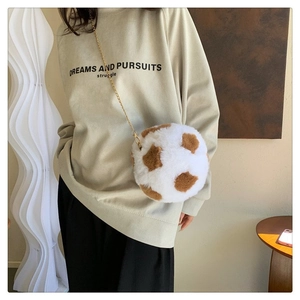 Detail of soft plush ball-shaped crossbody bag with cow print texture and golden chain