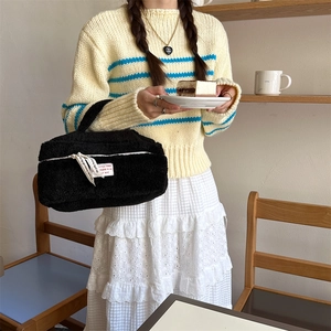 Detailed view of the black plush cosmetic bag held by a model in a cafe setting