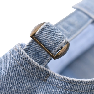 Close-up of adjustable bronze metal buckle on light blue washed denim baseball cap