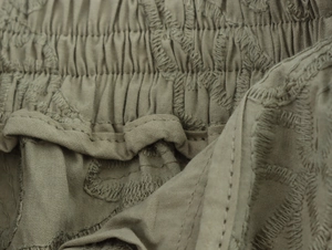 Close-up of olive green embroidered fabric detailing with elasticated waist texture