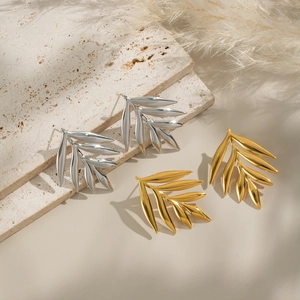 Macro view of gold and silver leaf earrings on a textured beige stone with pampas grass