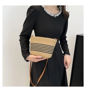 Detail of woven straw handbag with black stripes on model wearing a black dress