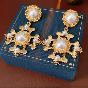 Dettaglio degli orecchini a croce vintage dorati con perle su un portagioie blu