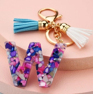 Macro shot of resin letter W keychain with colorful stones, blue and white tassels