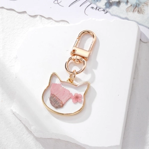 Detail of pink dried flowers inside cat-shaped gold metal frame keychain on white stone tray